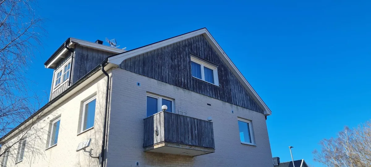 Samma hus före arbetet, med grå och väderbiten träpanel på gaveln och balkongen