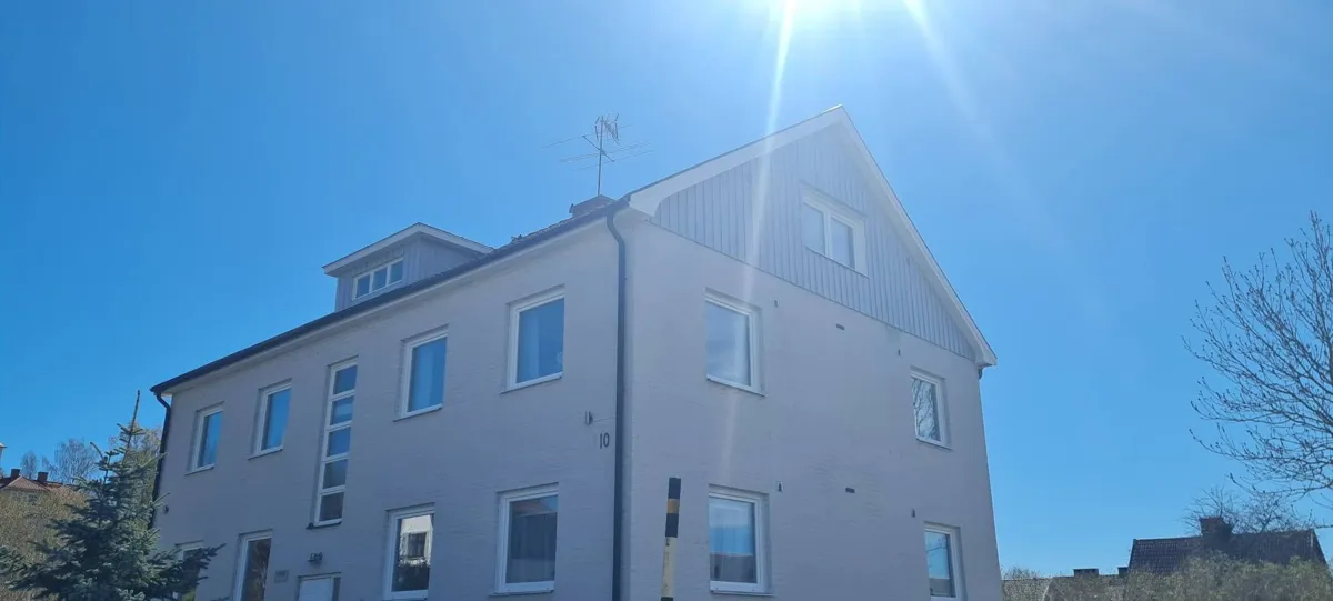 Ljust tegelhus med ljusgrå stående panel på gaveln mot en klarblå himmel
