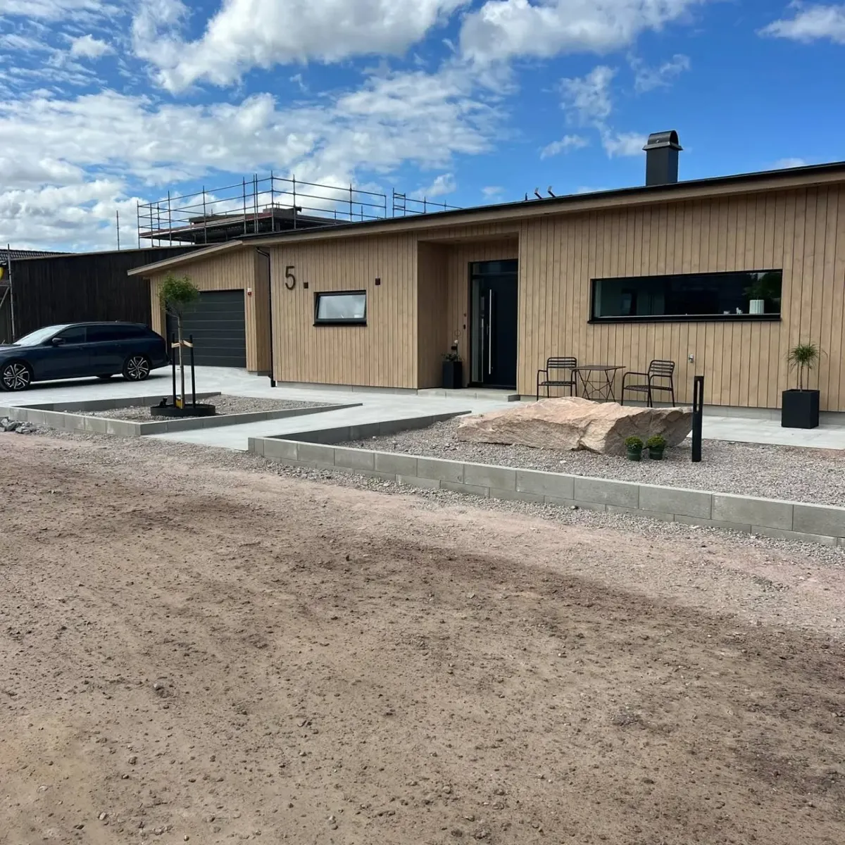 Villa med träfasad, plattsatt gång, kantsten av betongblock och grus framför entrén